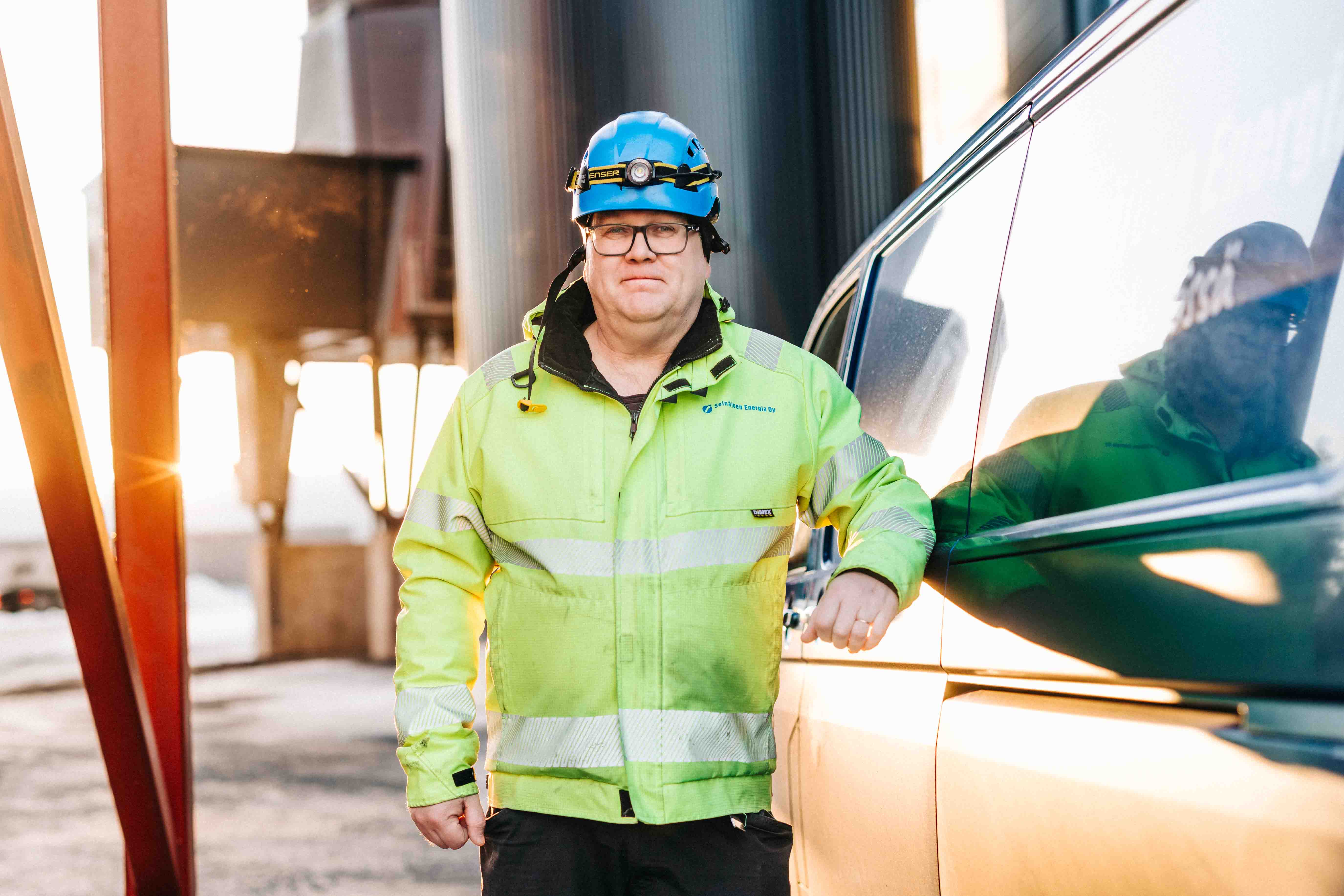 Kaukolämmön työntekijä nojaa autoon