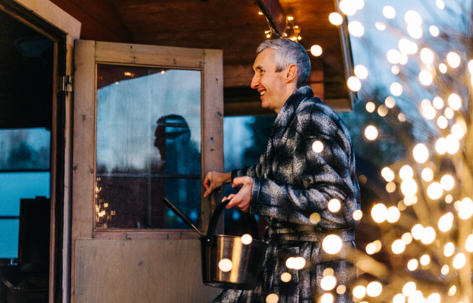 Mies menossa ulkosaunaan jouluvalojen valaistessa.